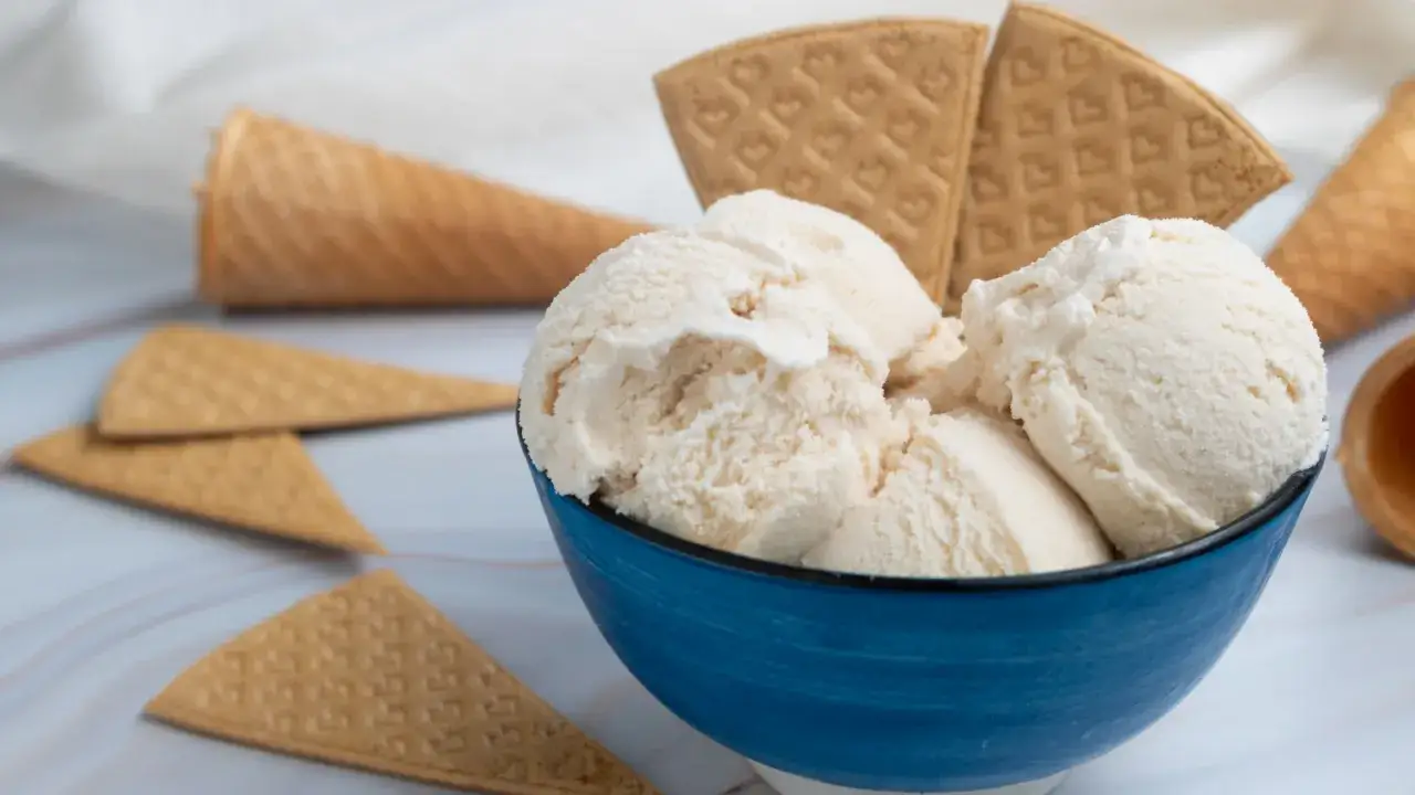 Coppetta blu con gelato artigianale ricetta perfetta, circondata da coni e cialde croccanti.