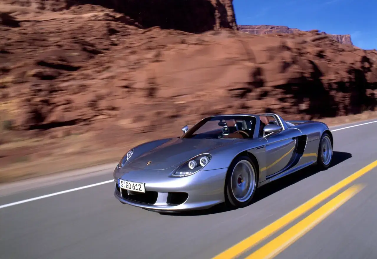 Srebrny Porsche Carrera GT pędzi pustynną drogą, otoczony surowymi, czerwonymi skałami.