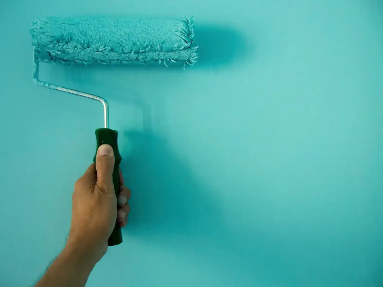 Main tenant une brosse à rouleau, il est en train de peindre une salle de bain en bleu turquoise.
