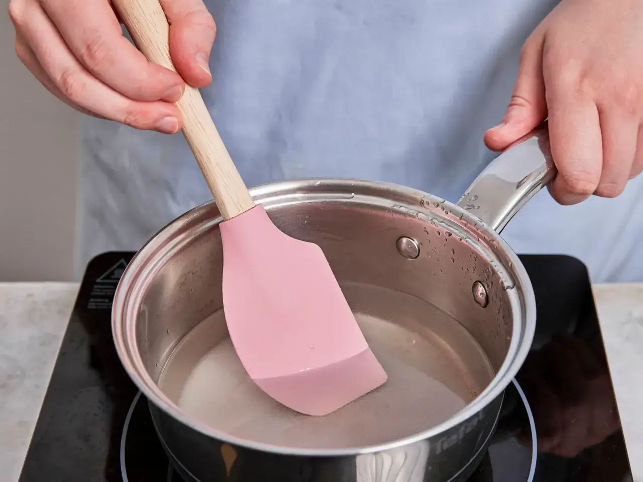 Zuckersirup selber machen: Eine rosa Spatel rührt in einem Topf auf dem Herd.