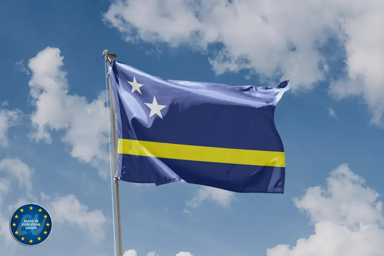 Flaga Curacao powiewa na wietrze na tle błękitnego nieba z chmurami.
