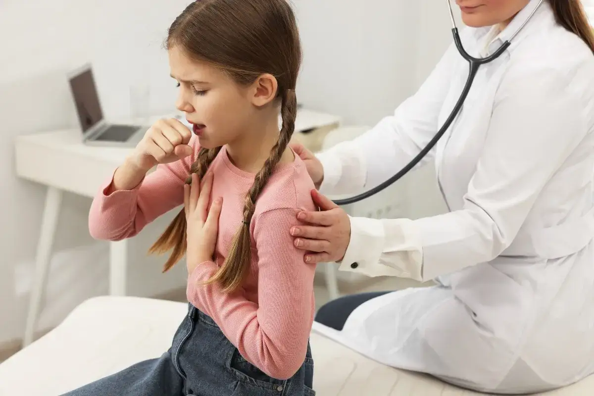 Bambina con trecce tossisce, appoggiando una mano sul petto. Un medico con stetoscopio la visita, preoccupato per i continui colpetti di tosse bambini.