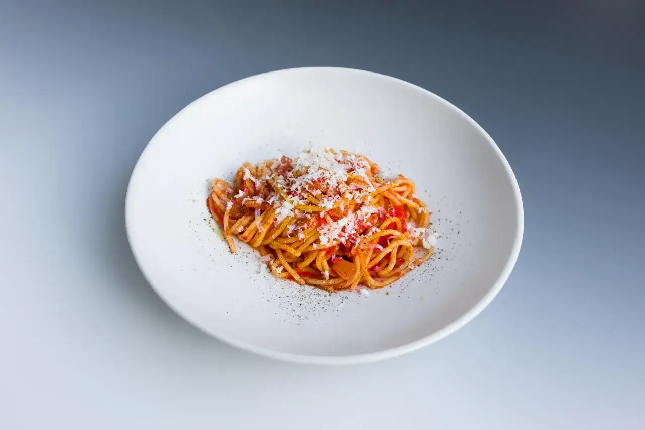 Ein Teller Spaghetti mit einer würzigen Tomatensoße, Guanciale und Pecorino-Käse – klassische Pasta Amatriciana.
