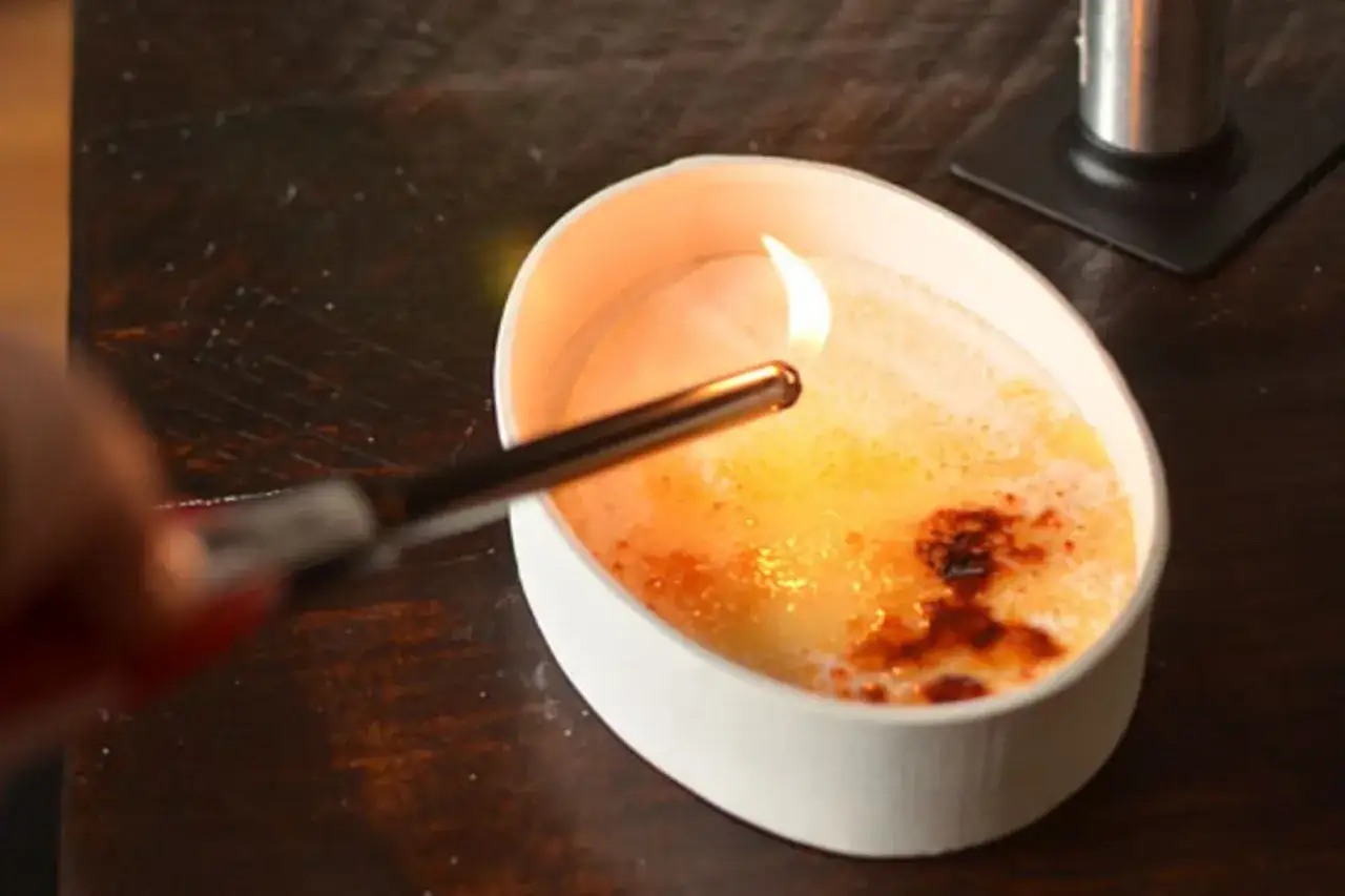 Creme brulee wird mit einem Brenner karamellisiert, die Zuckerschicht beginnt zu schmelzen und wird braun.