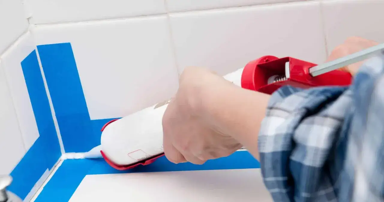 Application d'un joint époxy pour douche, avec du ruban bleu pour un résultat net.