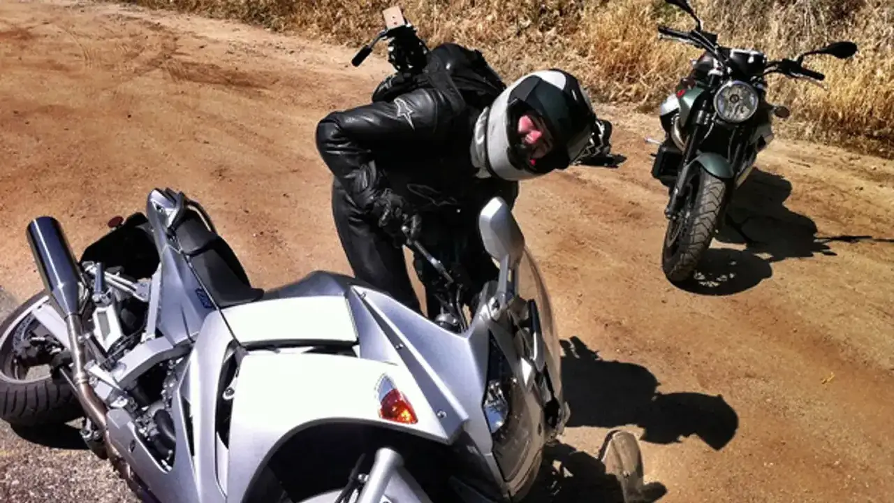 Motocyklista w czarnej skórze pochyla się nad srebrnym motocyklem Yamaha FJR. Obok stoi drugi motocykl.