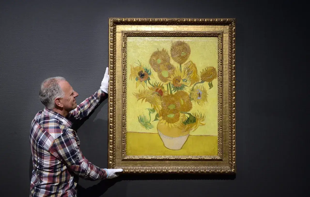 Mężczyzna w białych rękawiczkach prezentuje słoneczniki van Gogha oryginał w złotej ramie.