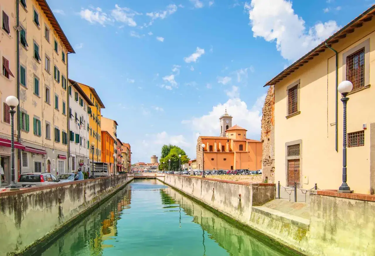 Canali e palazzi colorati nel quartiere Venezia di Livorno, con una chiesa arancione e un cielo azzurro pieno di nuvole.