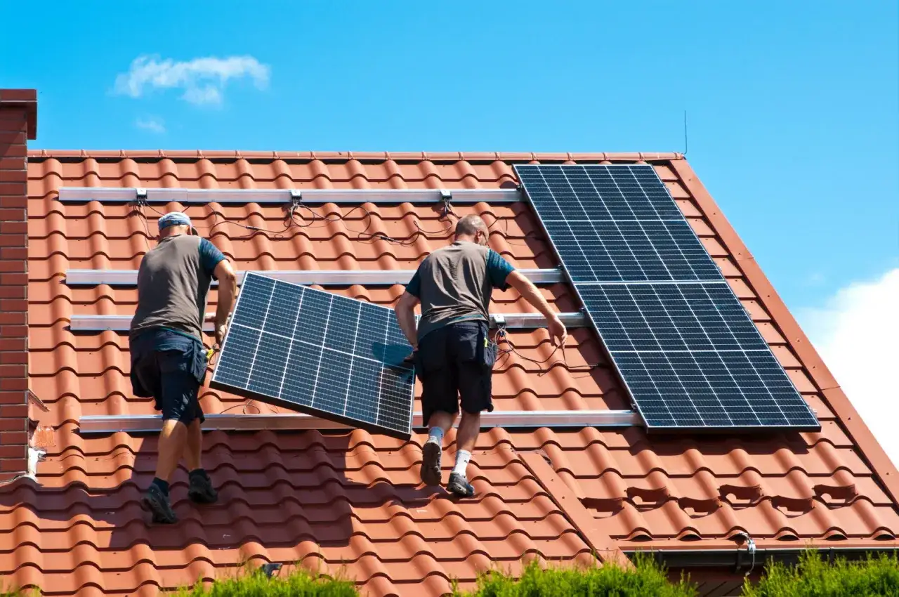 Deux ouvriers installent des panneaux solaires sur un toit. Ces panneaux servent à produire de l'électricité verte et renouvelable.