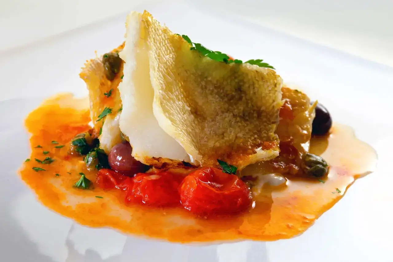 Delicioso bacalao encebollado con tomates, aceitunas y alcaparras en una salsa vibrante.