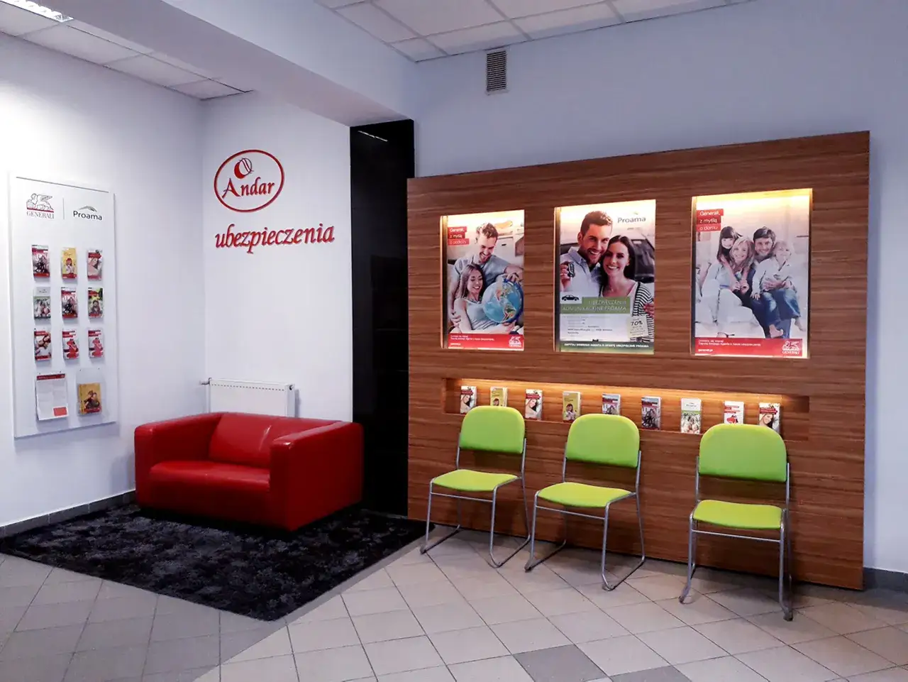Recepcja biura ubezpieczeniowego z czerwoną kanapą, zielonymi krzesłami i plakatami reklamowymi.
