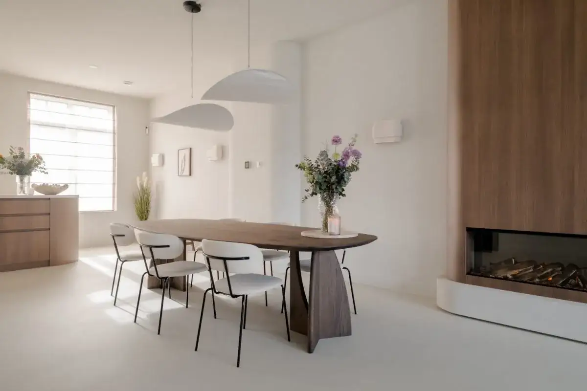 Een sfeervol feng shui huis met een ruime eettafel, witte stoelen, een moderne haard en een boeket bloemen.