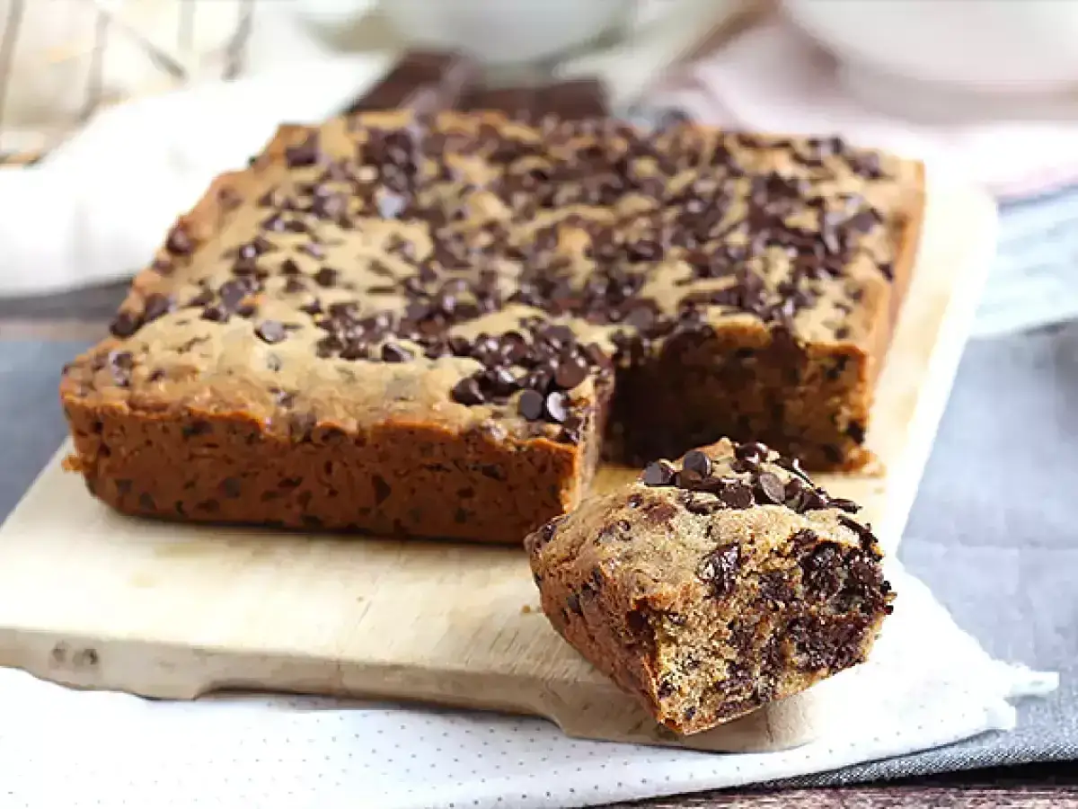 En stor, fyrkantig chocolate chip cookie med en bit borttagen, som visar saftigt inre.