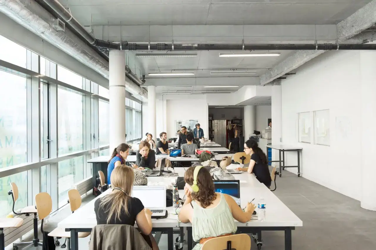 Des étudiants travaillent dans un espace ouvert, peut-être une école d'art, avec des bureaux et des ordinateurs. Le **ensaama classement** est visible sur les vitres.
