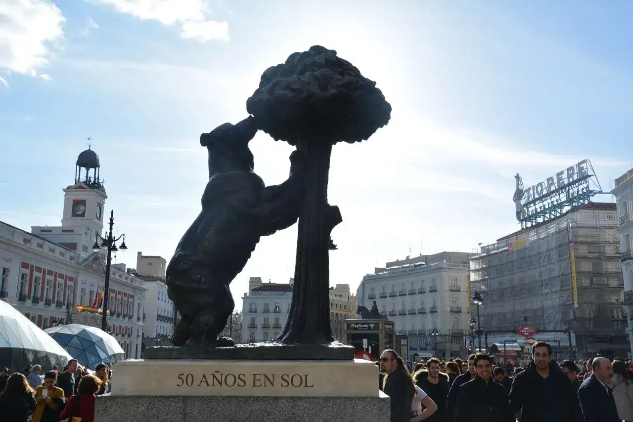 El Oso y el Madroño, un símbolo de Madrid en un día soleado. Gente pasea por la plaza.
