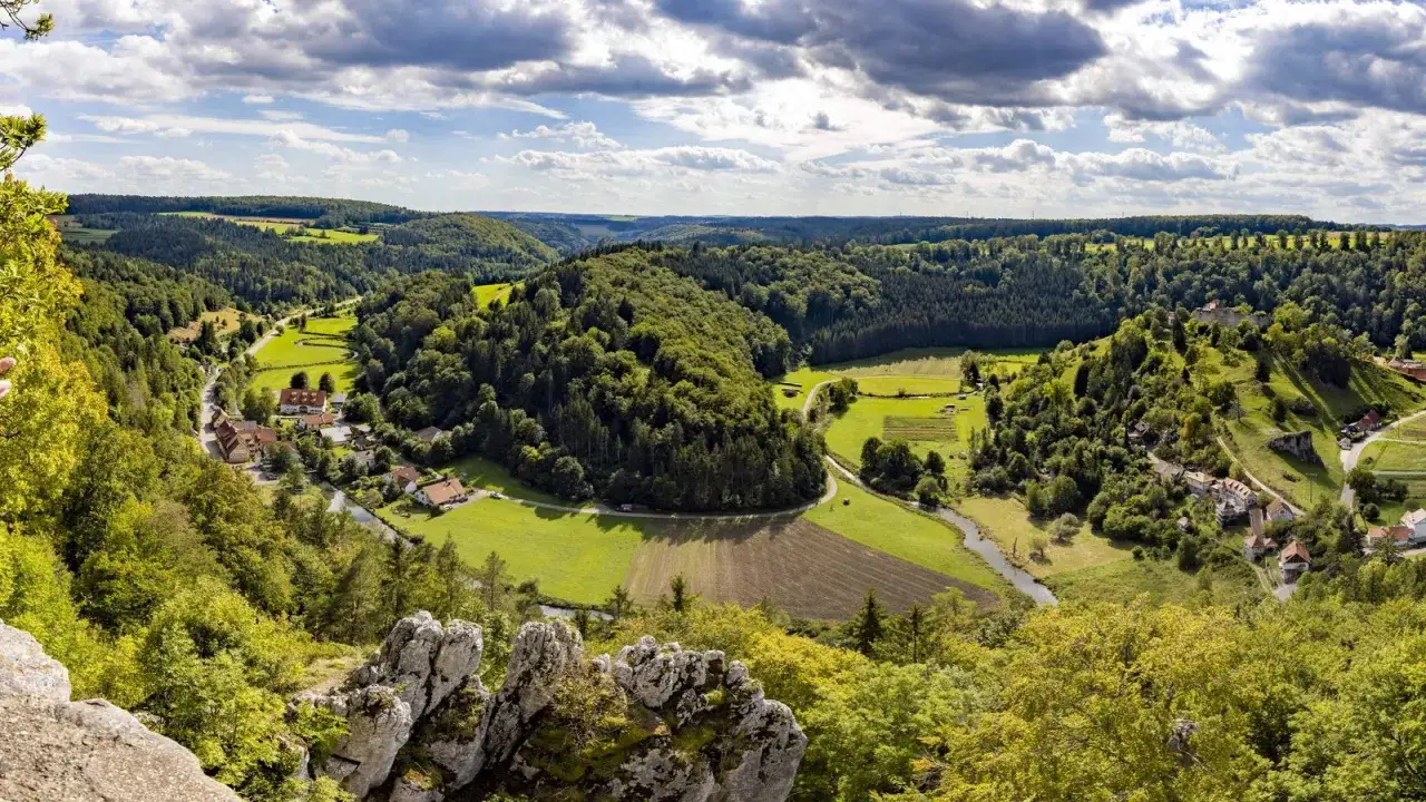 Blick ins Grüne: Ein malerisches Tal mit Häusern, Feldern und einem Fluss lädt zum Odenwald Wandern ein.