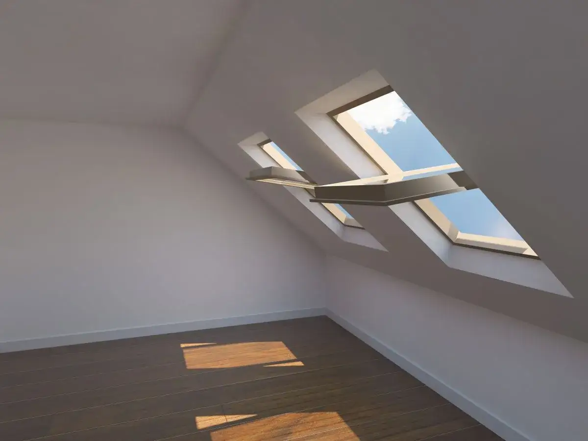 Interno di una mansarda con finestre sul tetto che illuminano il pavimento in legno.