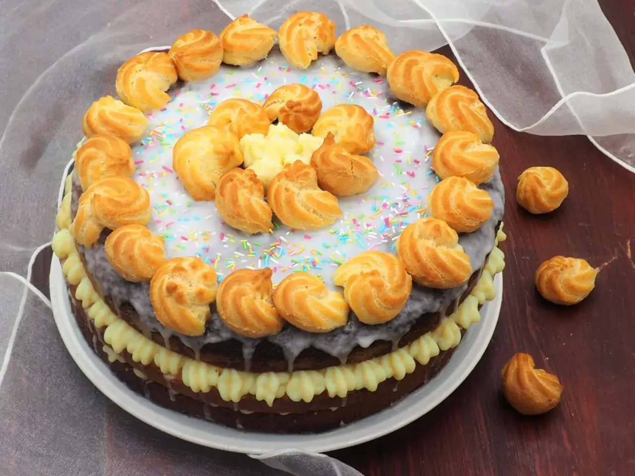 Torta decorata con bignè e crema al latte, spolverata di codette colorate.