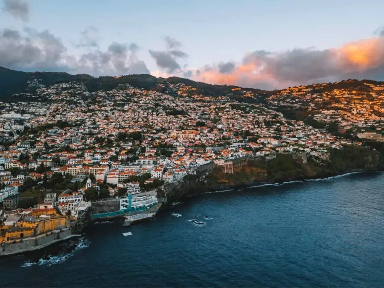 Widok na Funchal, Madera. Listopadowa pogoda zachwyca ciepłymi barwami zachodzącego słońca, oświetlając zbocza gór porośnięte domami.