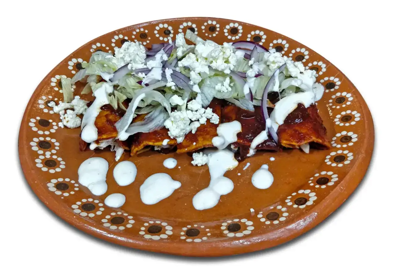 Enchiladas, en typisk guatemalansk r&auml;tt, serveras p&aring; en vackert dekorerad lertallrik med ost, sallad och l&ouml;k.