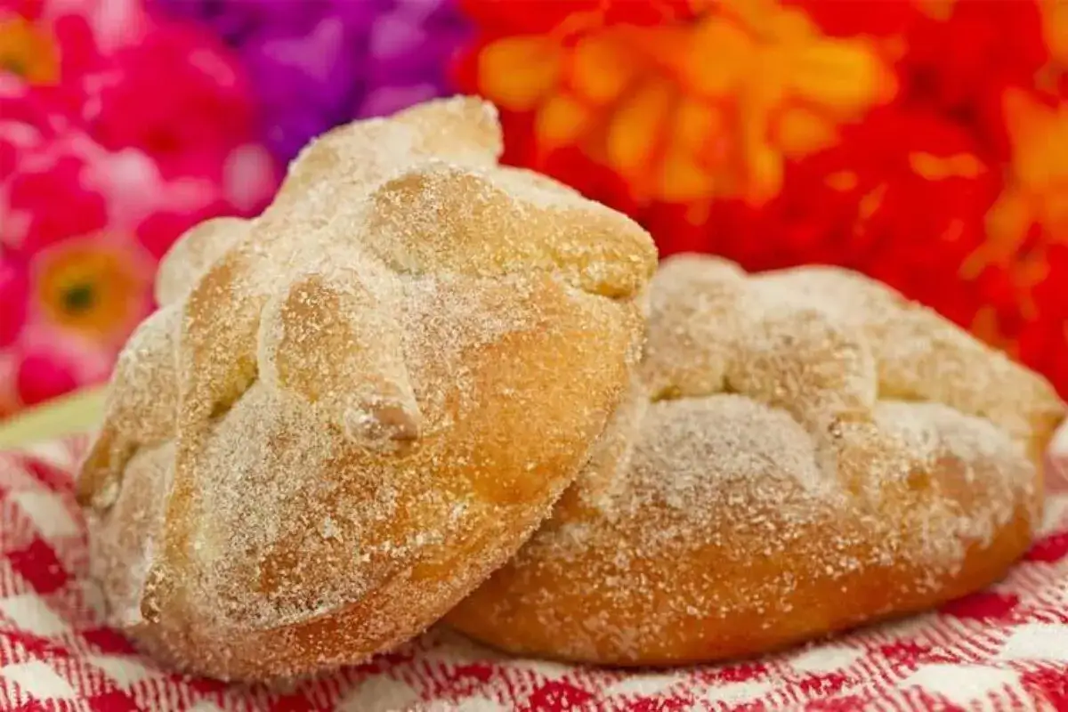 Dos panes de muerto cubiertos de az&uacute;car, con flores de cempas&uacute;chil y terciopelo al fondo.