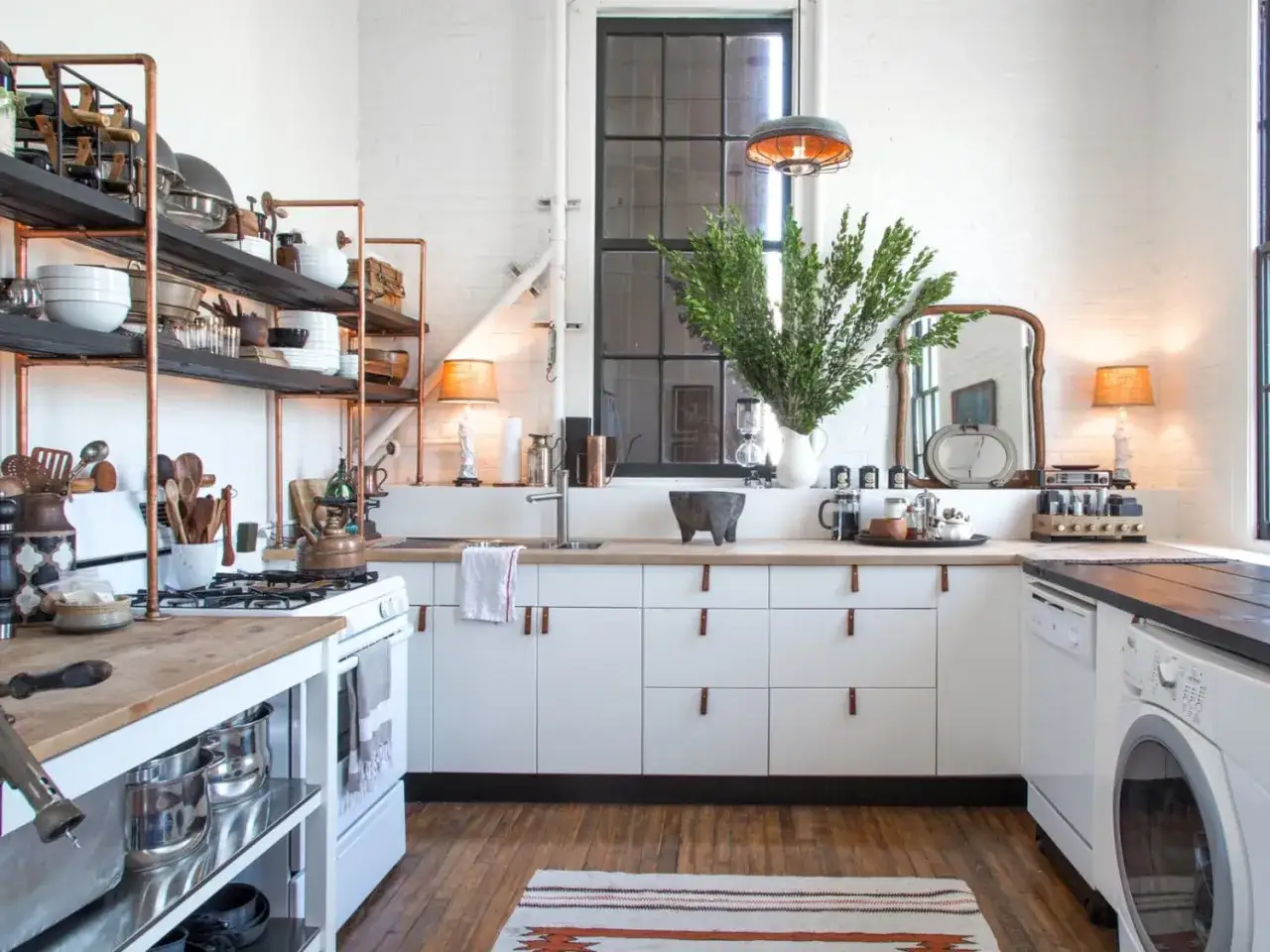Cocina r&uacute;stica con tirador cuero en los cajones blancos. Estanter&iacute;as de cobre y madera, electrodom&eacute;sticos vintage y plantas verdes.