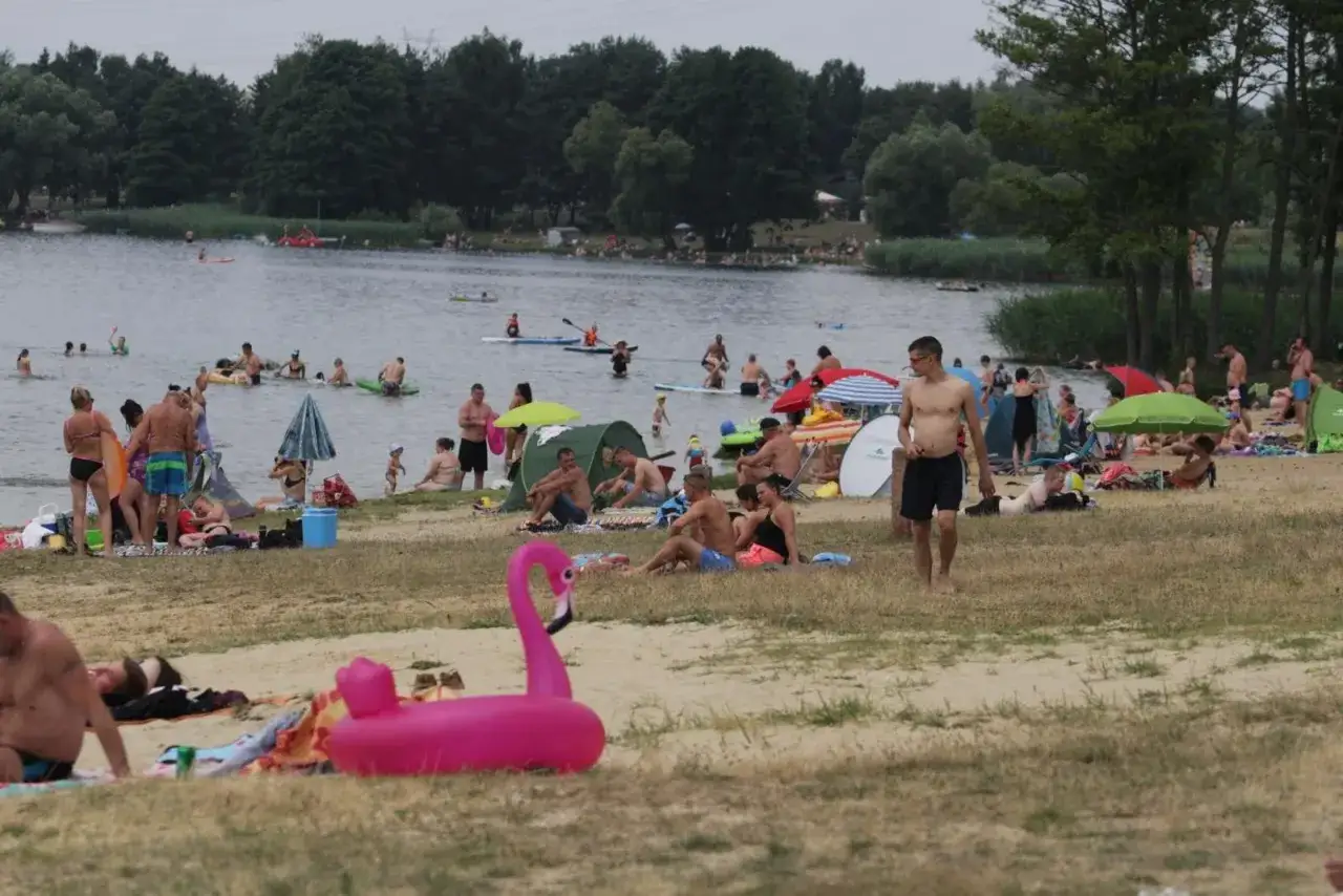 Pławniowice jezioro tętni życiem. Ludzie kąpią się, opalają i relaksują na plaży, ciesząc się letnim dniem.