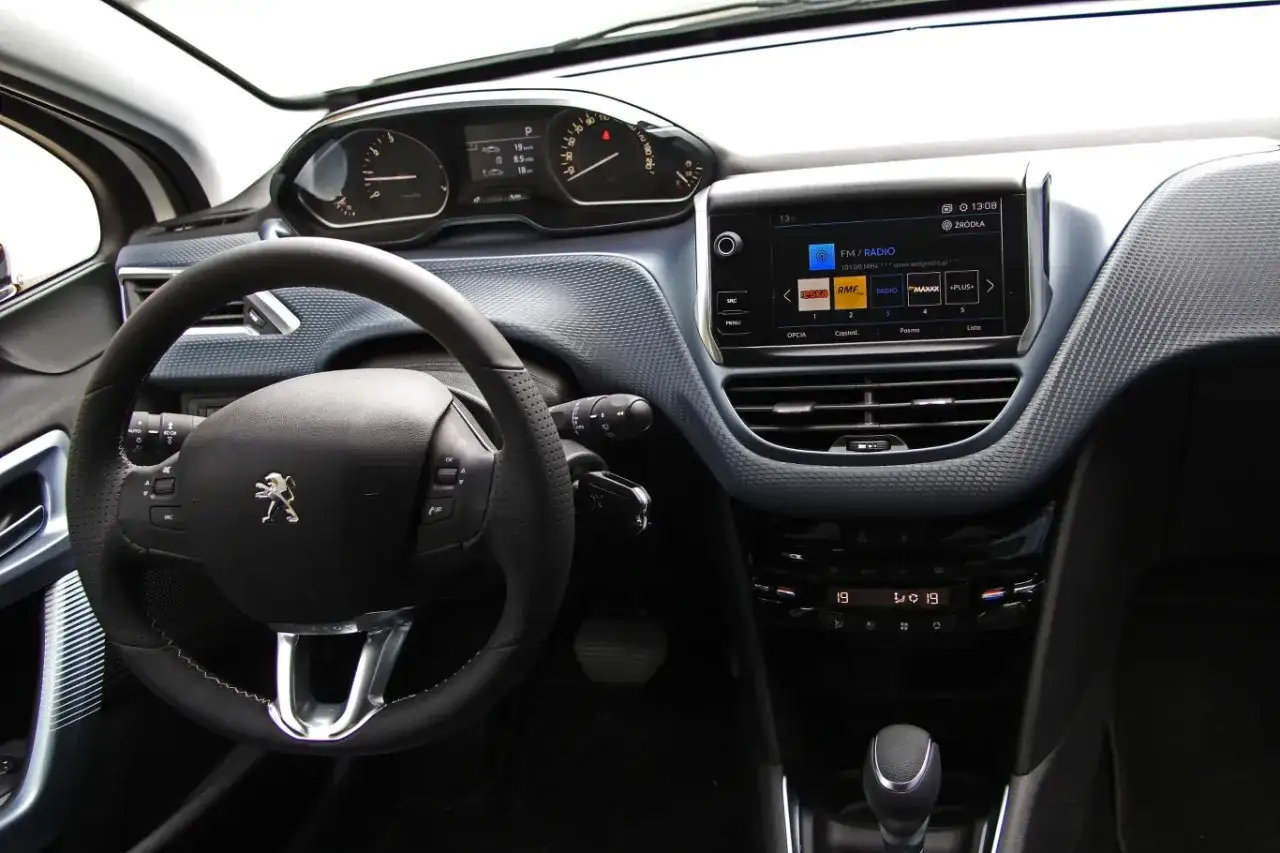 Wnętrze Peugeot e-208: kierownica, cyfrowe zegary i ekran multimedialny z radiem.