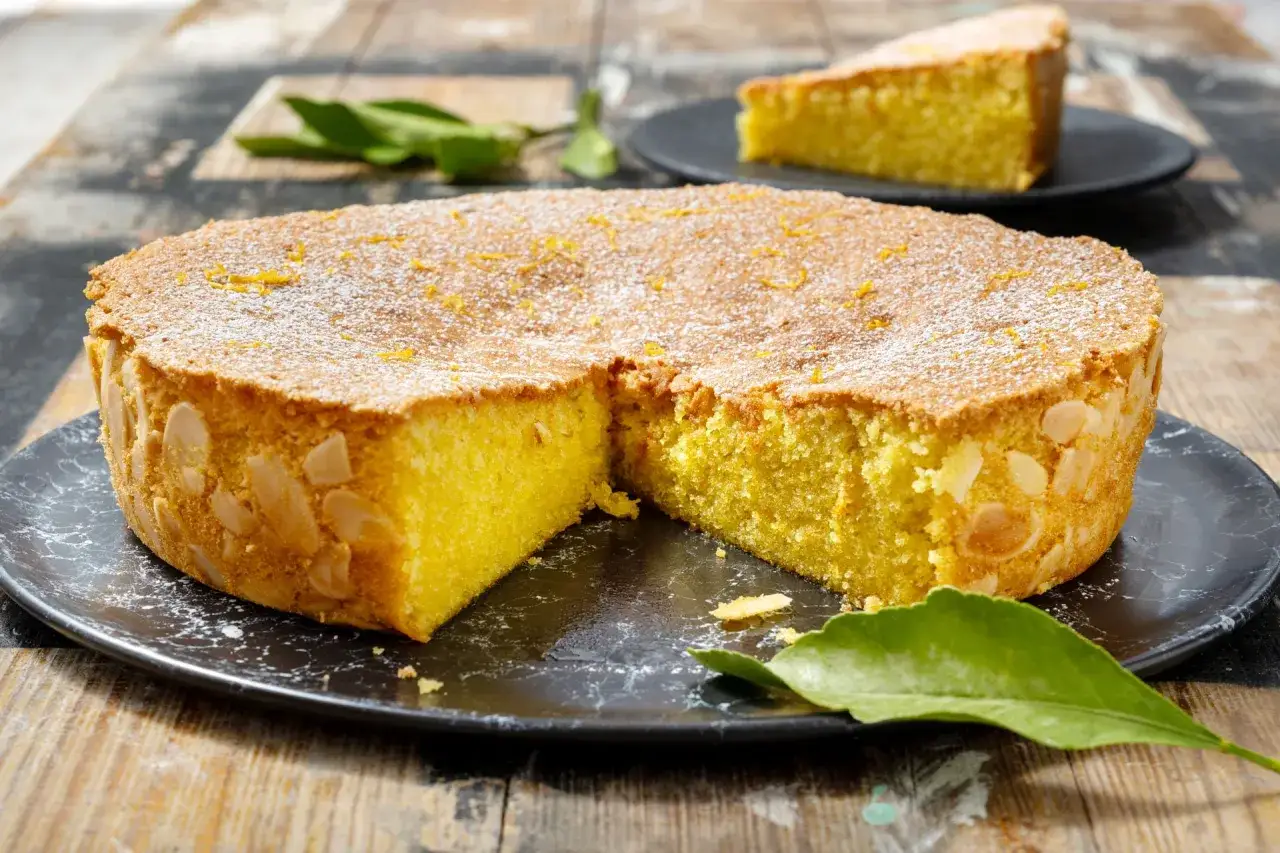 Torta soffice caprese al limone, decorata con mandorle e zucchero a velo, su un piatto scuro.