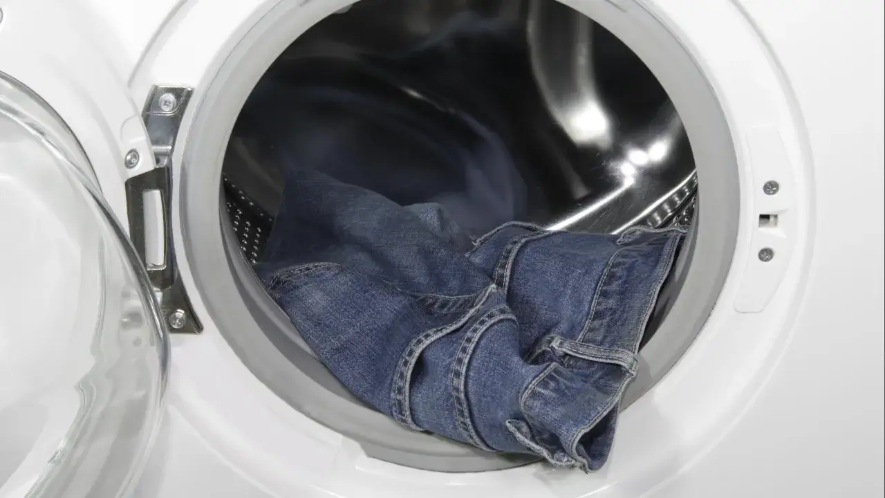 Blaue Jeans liegen in der Trommel einer Waschmaschine, bereit, um sie einlaufen zu lassen.