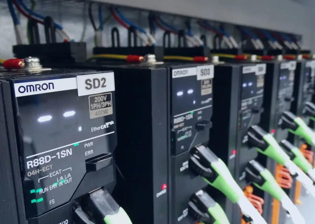 Rzędy modułów PLC OMRON SD2 i SD3 z zielonymi kablami.