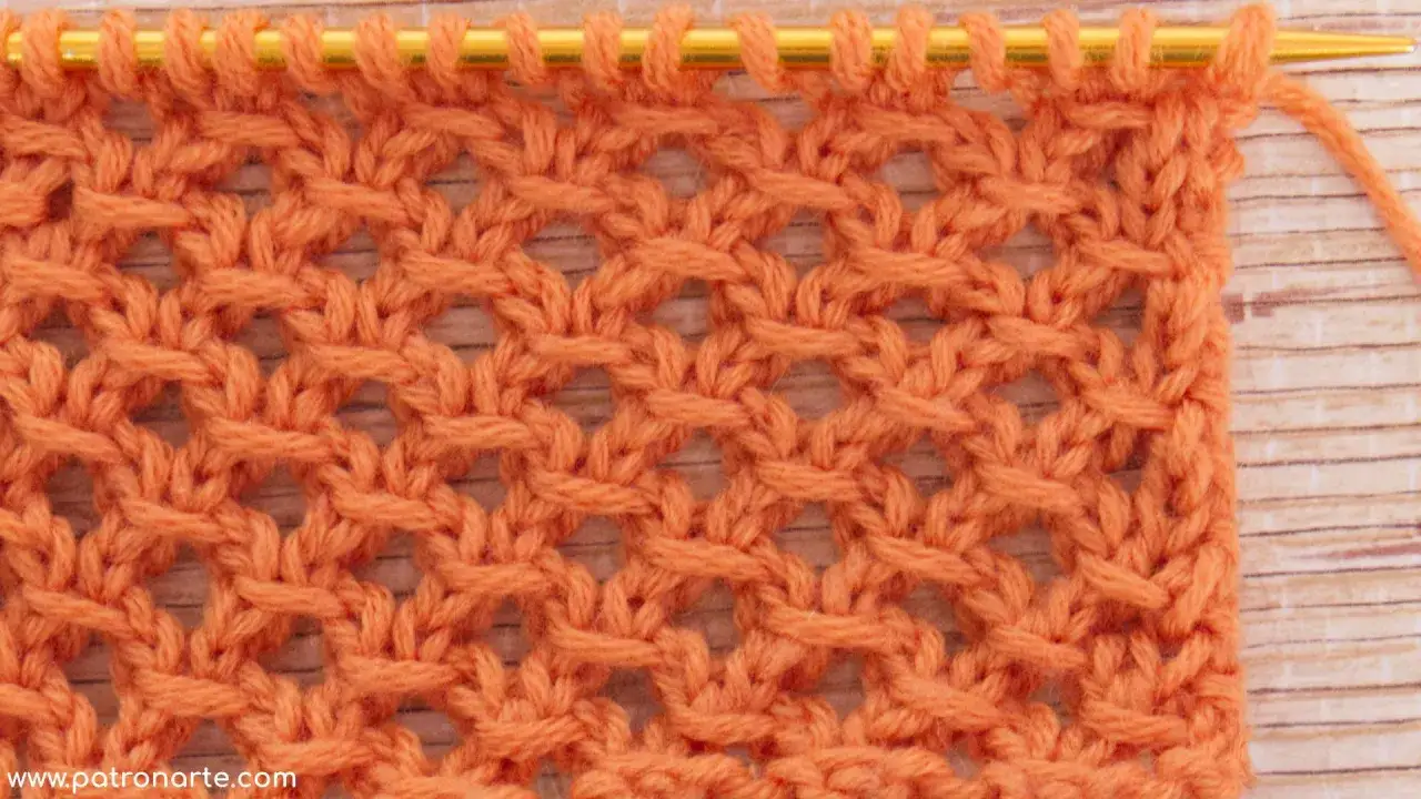Muestra de puntos calados a dos agujas utilisima, un tejido de encaje naranja con un patr&oacute;n de rombos abiertos.