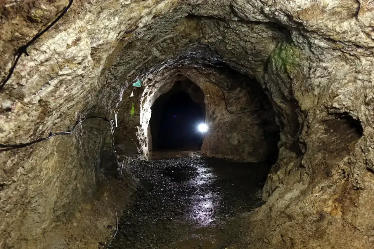 Wnętrze kopalni w Kletnie. Kamienne ściany, mokra posadzka i światło latarki wiodące w głąb ciemnego tunelu.