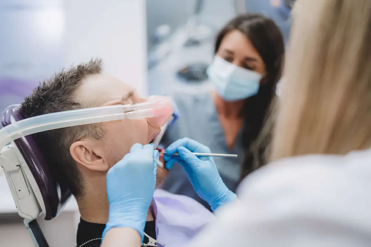 Pacjent z maską gazową podczas zabiegu stomatologii zachowawczej. Dentysta w rękawiczkach pracuje przy jego zębach.