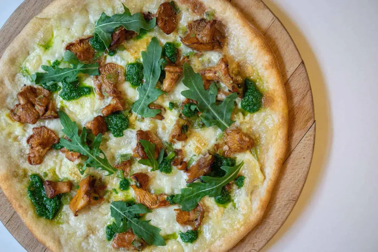 Pizza z kurkami, serem i zielonym pesto, udekorowana rukolą. Idealna na jesienny obiad.