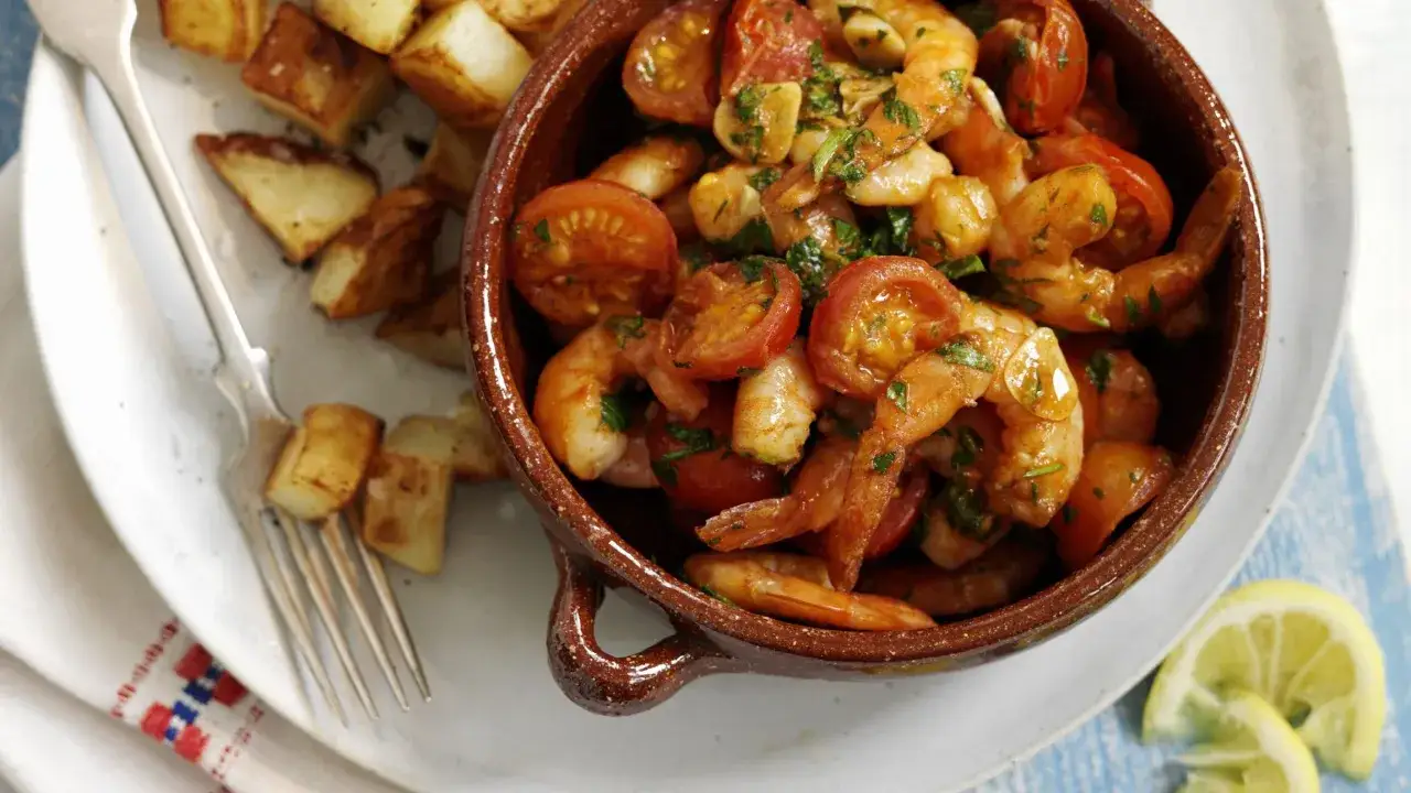 Deliziosa catalana di gamberi con pomodorini e aglio, accompagnata da patate arrosto e spicchi di limone.