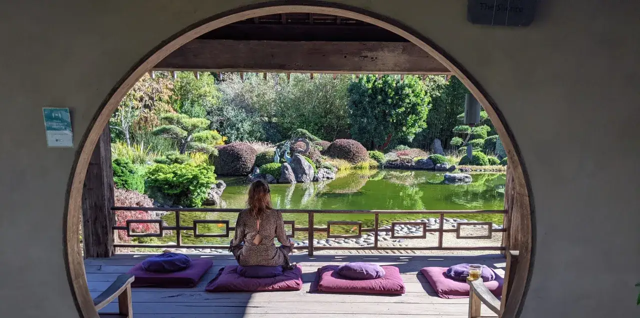 Kvinna mediterar vid en damm i en japansk trädgård, söker inre lugn.