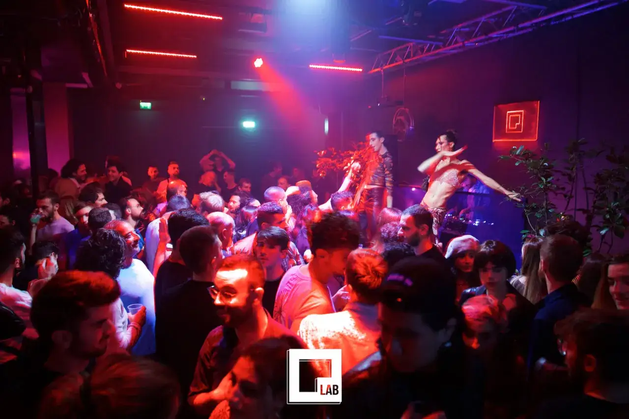 Folla in un locale notturno a Milano, con artisti sul palco e luci rosse. Atmosfera vibrante al qclub milano.