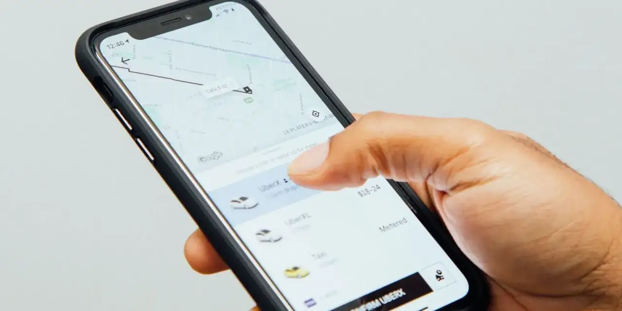 Dłoń wybiera przejazd w aplikacji Uber. Widoczna mapa i opcje: UberX, UberXL, Taxi.
