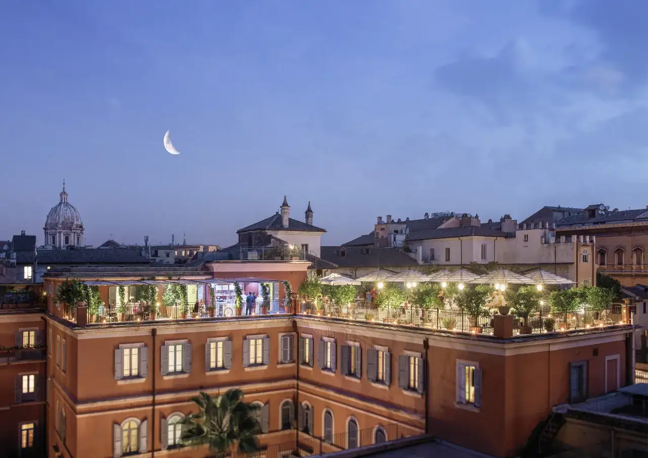 Vue du toit-terrasse animé du **hotel Ponte Sisto Rome** sous un ciel crépusculaire avec une lune en croissant.