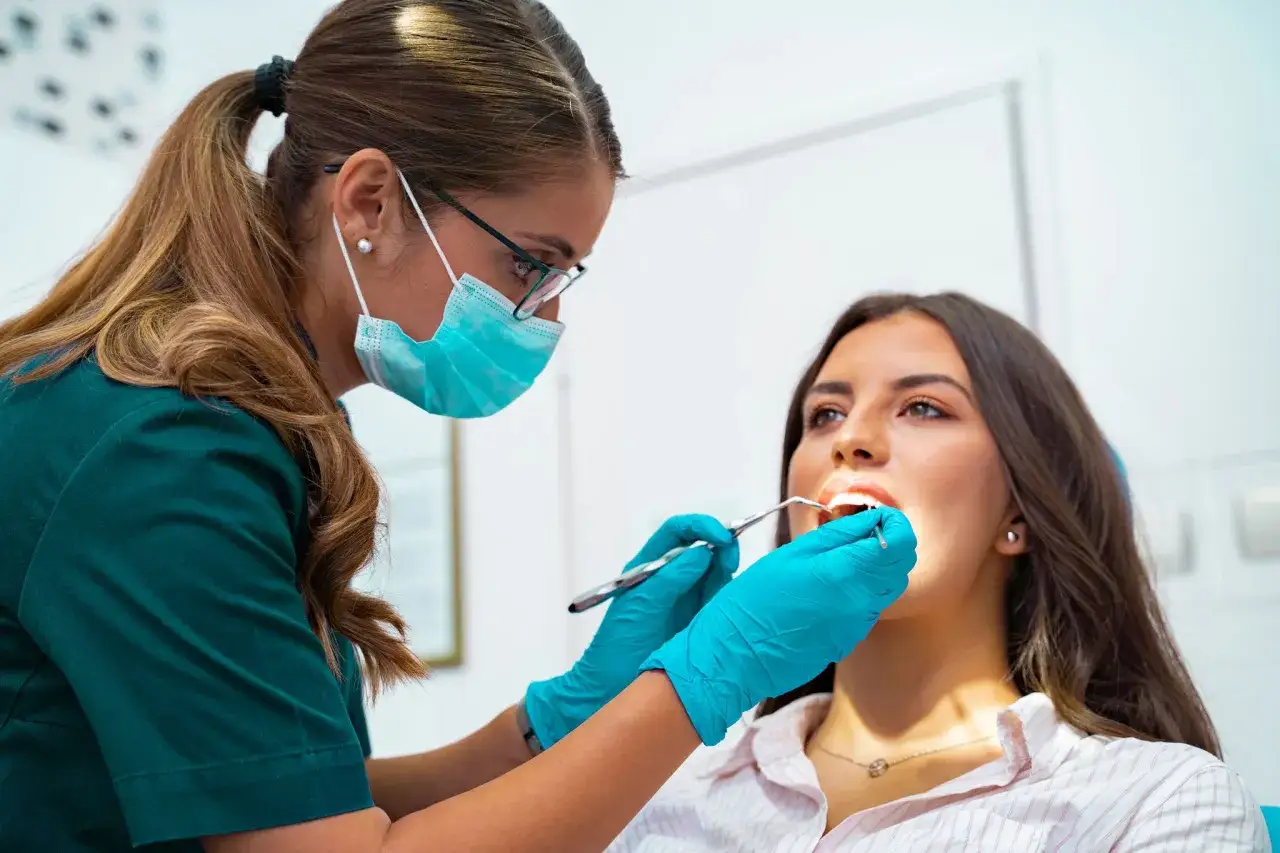 Dentystka w masce i rękawiczkach bada zęby pacjentki. Zastanawiasz się, ile trwa wyrywanie 8 zęba?