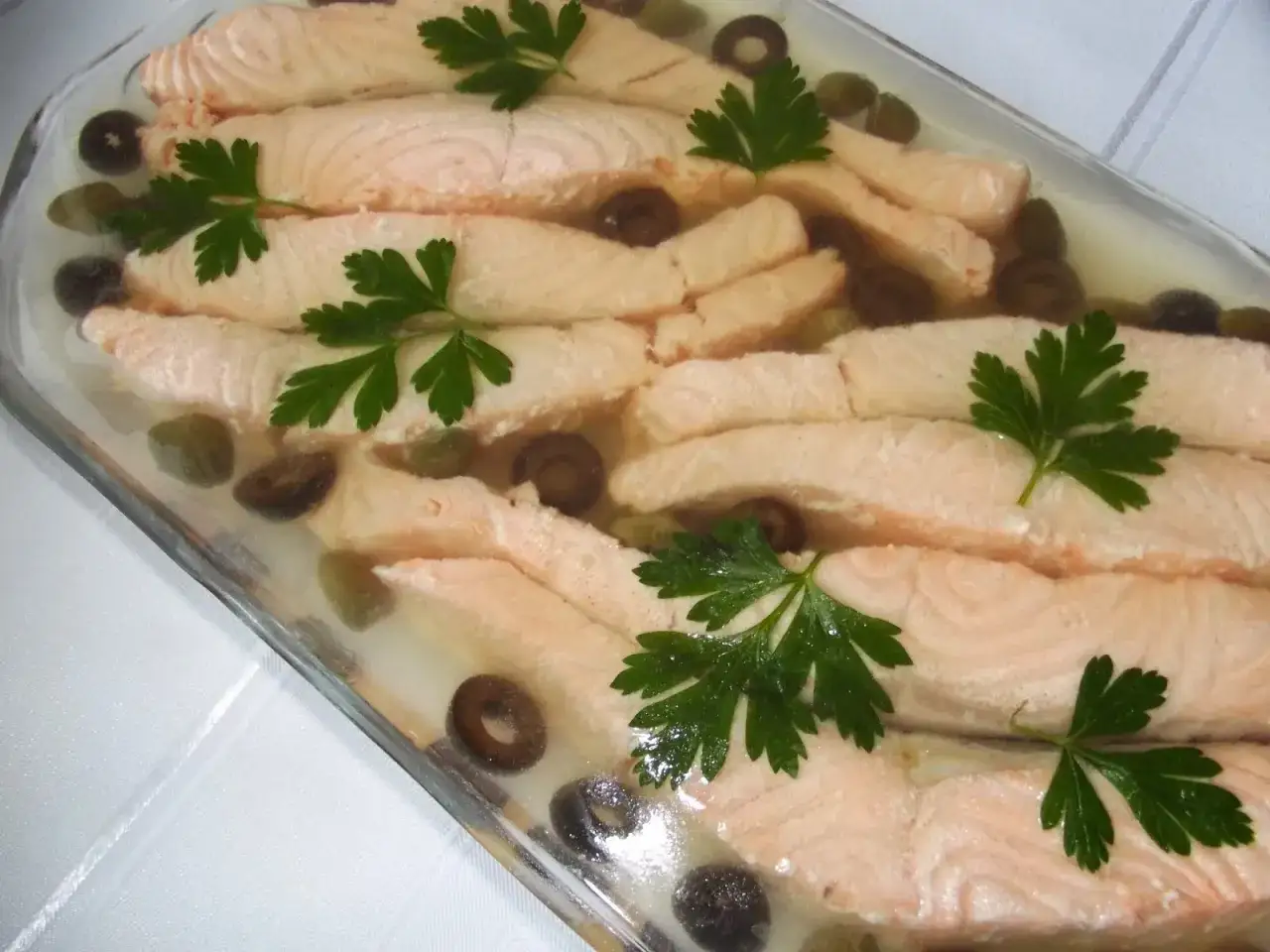 Łosoś w galarecie z oliwkami i kaparami, ozdobiony natką pietruszki. Elegancka przystawka na specjalne okazje.