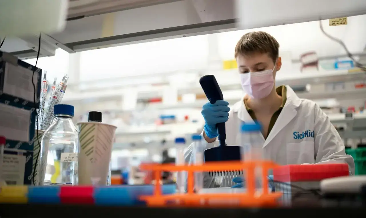 Ricercatore in laboratorio, con camice e mascherina, lavora con pipette. La ricerca sulla fibrosi cistica come si scopre &egrave; fondamentale.
