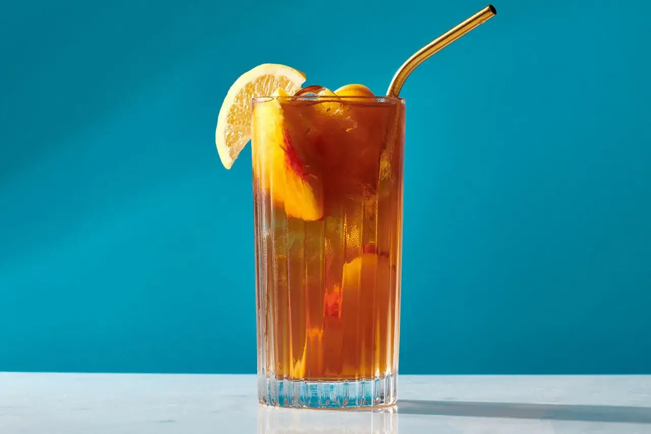 Orzeźwiający drink z ice tea, brzoskwinią i plasterkiem cytryny, ozdobiony złotą słomką.