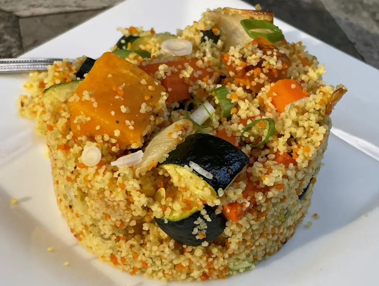 Cuscus con verduras, un plato colorido con calabaza, calabacín y zanahoria, adornado con cebolleta.