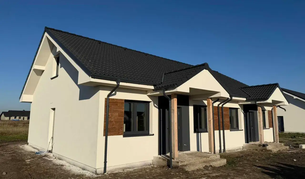 Nowy dom z czarnym dachem i jasną elewacją, gotowy na mieszkanie za remont.