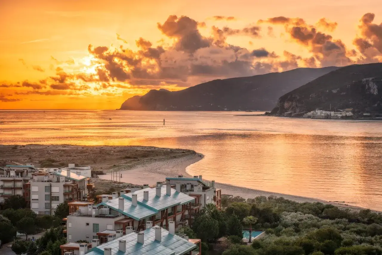 Goldener Sonnenuntergang über dem Setubal Strand. Häuser mit türkisfarbenen Dächern blicken auf das Meer.