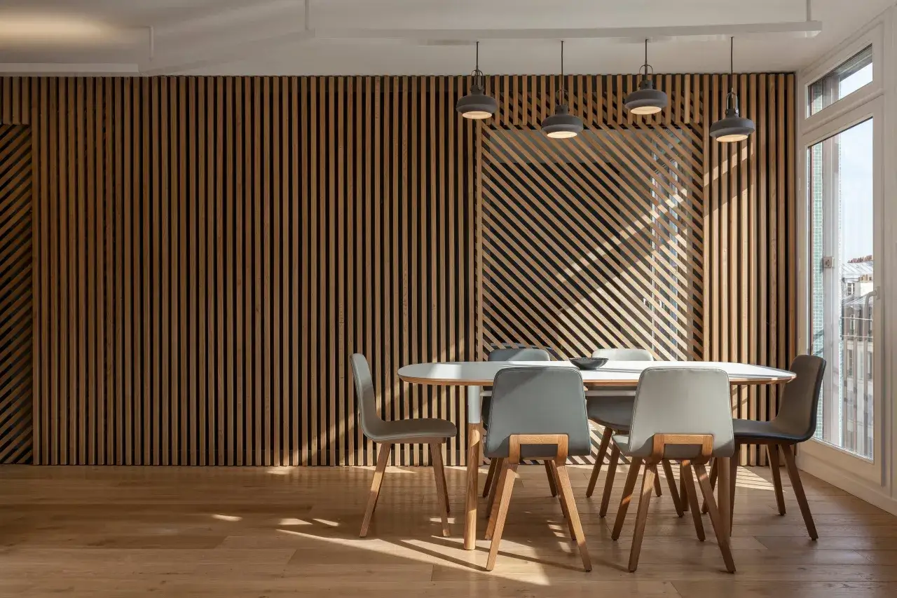 Un elegante soggiorno con un'impressionante parete in **parquet a parete** a listelli verticali e diagonali. Tavolo bianco con sedie grigie.