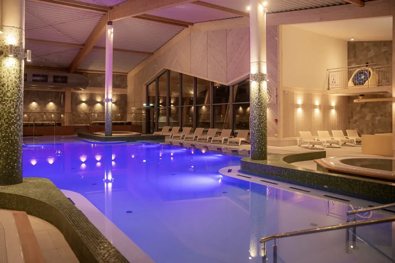 Relaks w basenie z podświetleniem w Aries Szczyrk. Woda lśni fioletem, a wok&oacute;ł leżaki i jacuzzi zapraszają do odpoczynku.