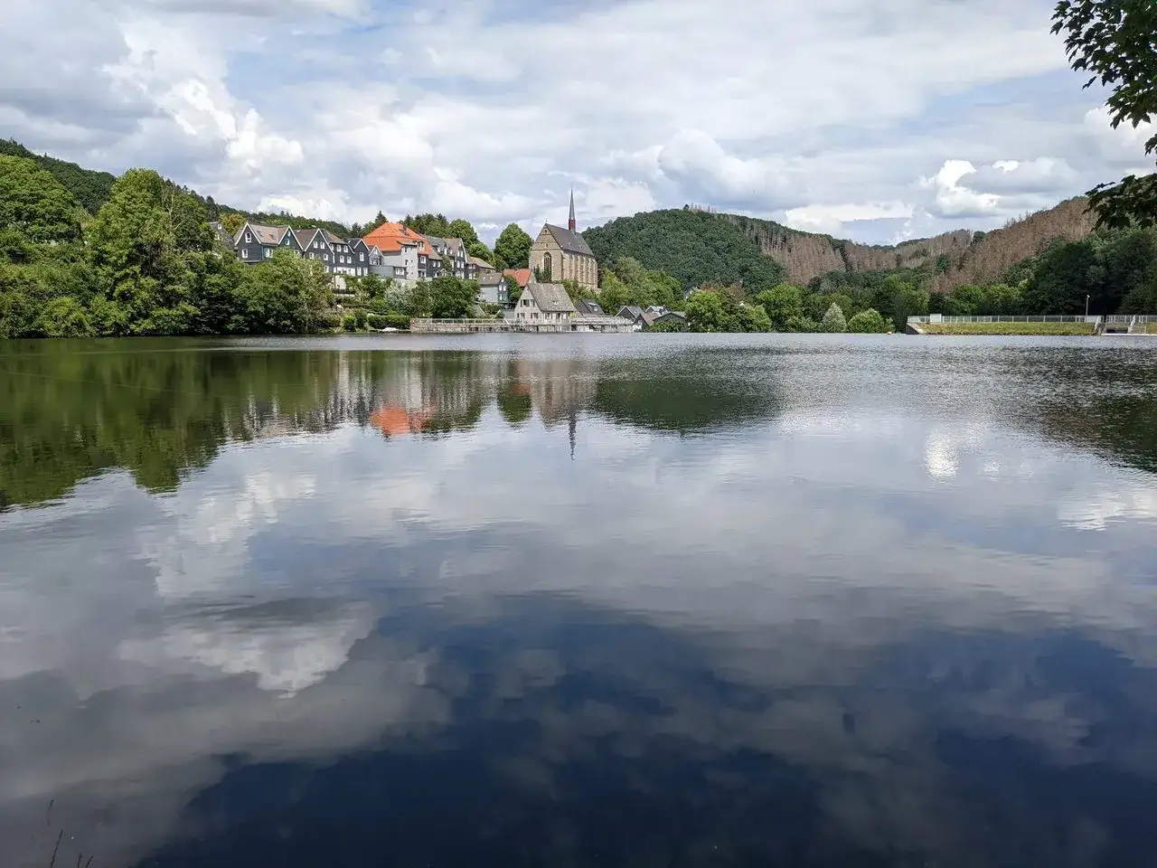 Spiegelglatte Wasserfl&auml;che des Beyenburger Stausees mit reflektierten Wolken und H&auml;usern. Ein idyllischer Ort f&uuml;r eine Rundweg-Wanderung.